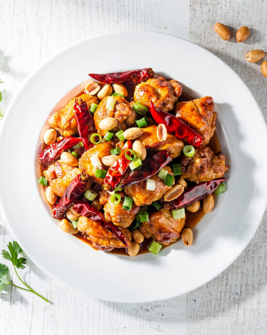 A vibrant, glossy plate of homemade kung pao chicken with crispy chicken, roasted peanuts, and dried chiles.
