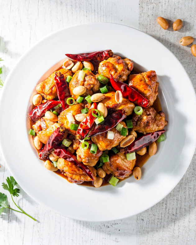 A vibrant, glossy plate of homemade kung pao chicken with crispy chicken, roasted peanuts, and dried chiles.