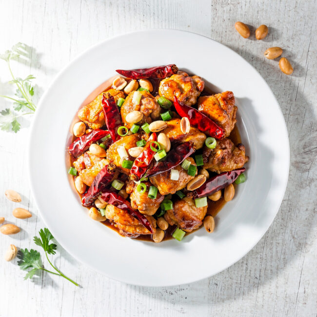 A vibrant, glossy plate of homemade kung pao chicken with crispy chicken, roasted peanuts, and dried chiles.