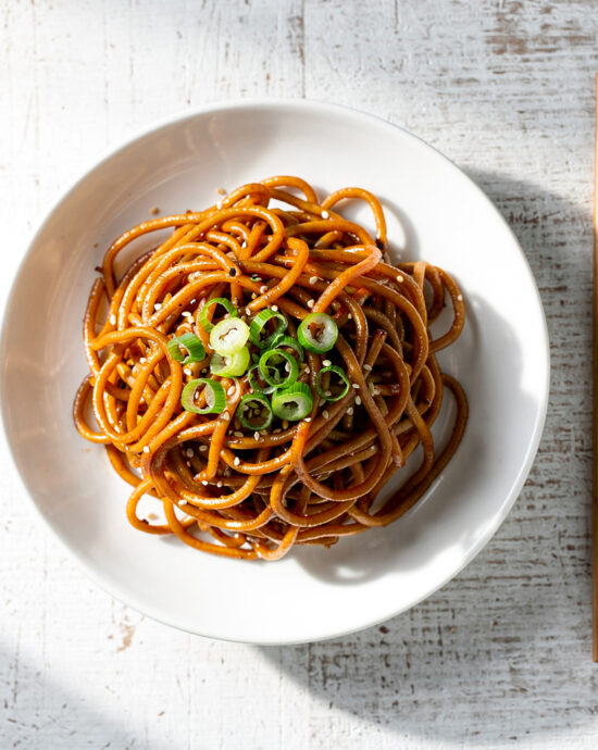 A vibrant, glossy pile of lo mein noodles tossed with colorful vegetables in a shallow white bowl.