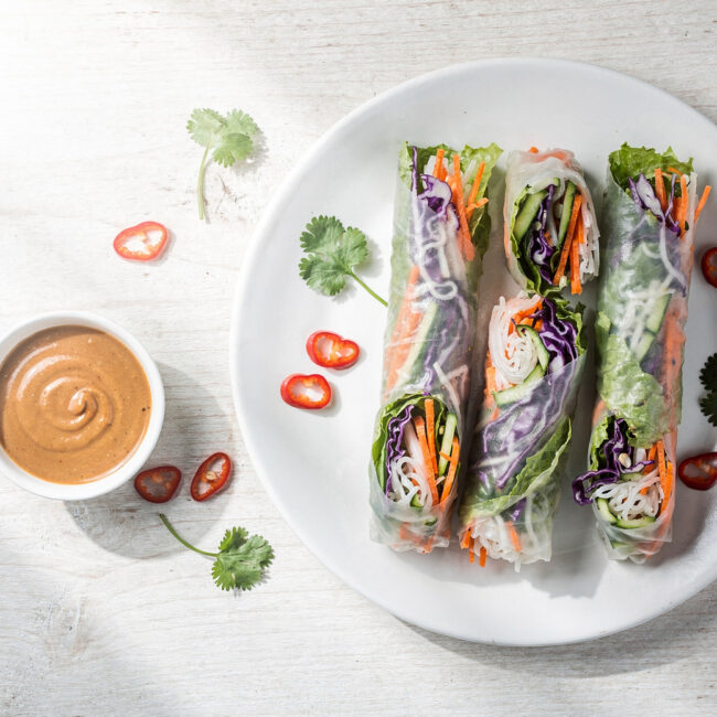 Golden, crispy spring rolls recipe served on a rustic wooden board with vibrant dipping sauce.