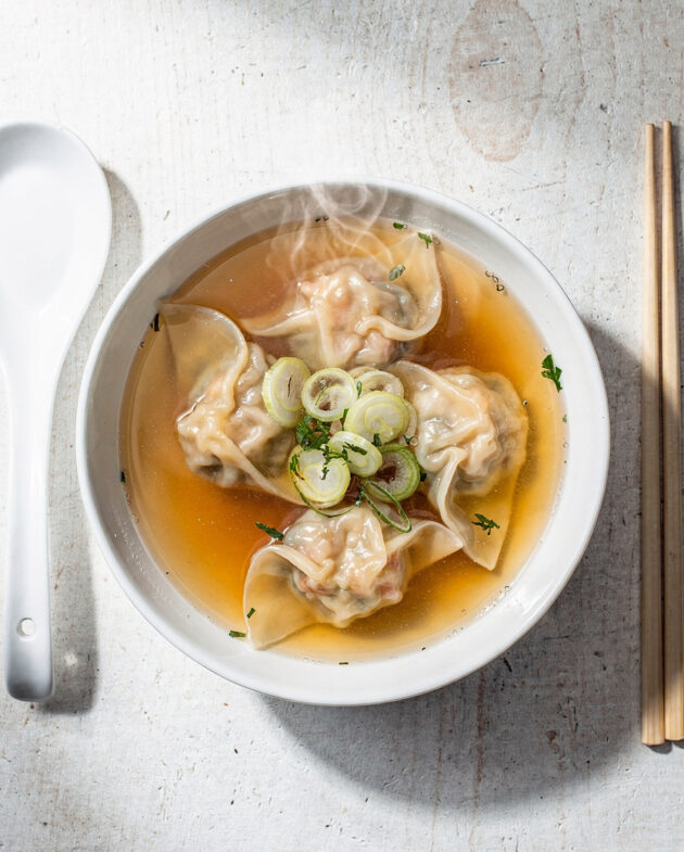 A beautifully styled bowl of our homemade wonton soup recipe, featuring plump dumplings and a clear, aromatic broth.