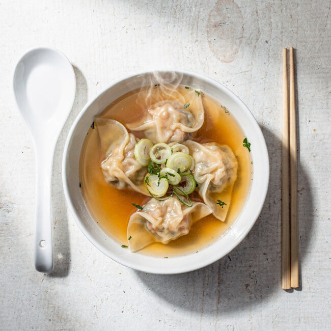 A beautifully styled bowl of our homemade wonton soup recipe, featuring plump dumplings and a clear, aromatic broth.