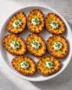 Eight crispy loaded potato skins with melted cheddar, sour cream, and chives on a white plate.